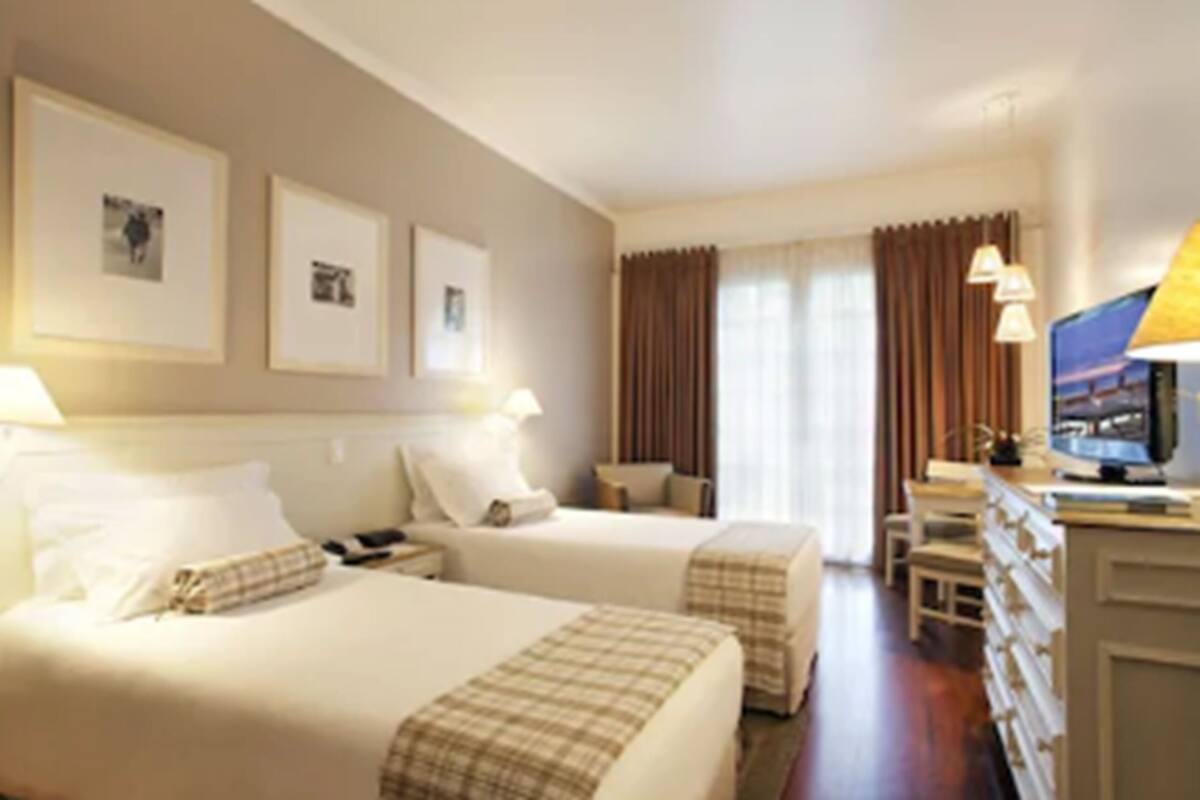 Habitación de hotel con dos camas, un escritorio, un televisor y una ventana con cortinas.