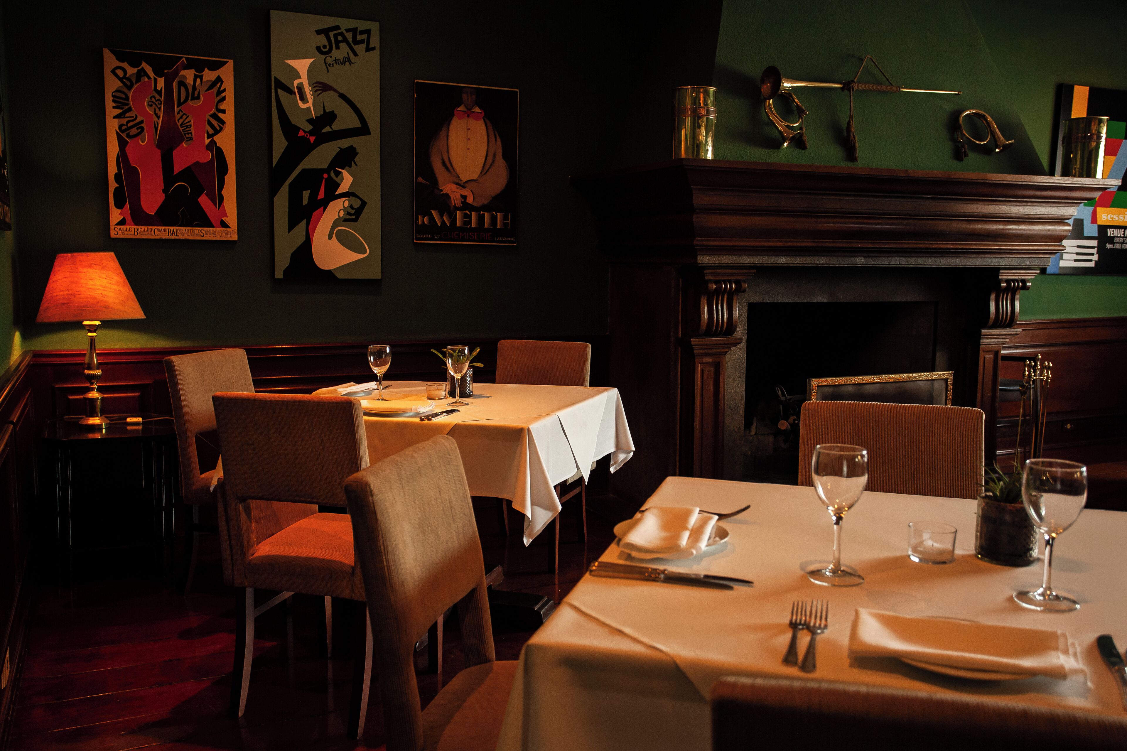 A dimly lit restaurant with tables set for dining, a fireplace, and artwork on the walls.