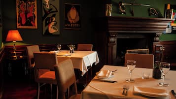 A dimly lit restaurant with tables set for dining, a fireplace, and artwork on the walls.