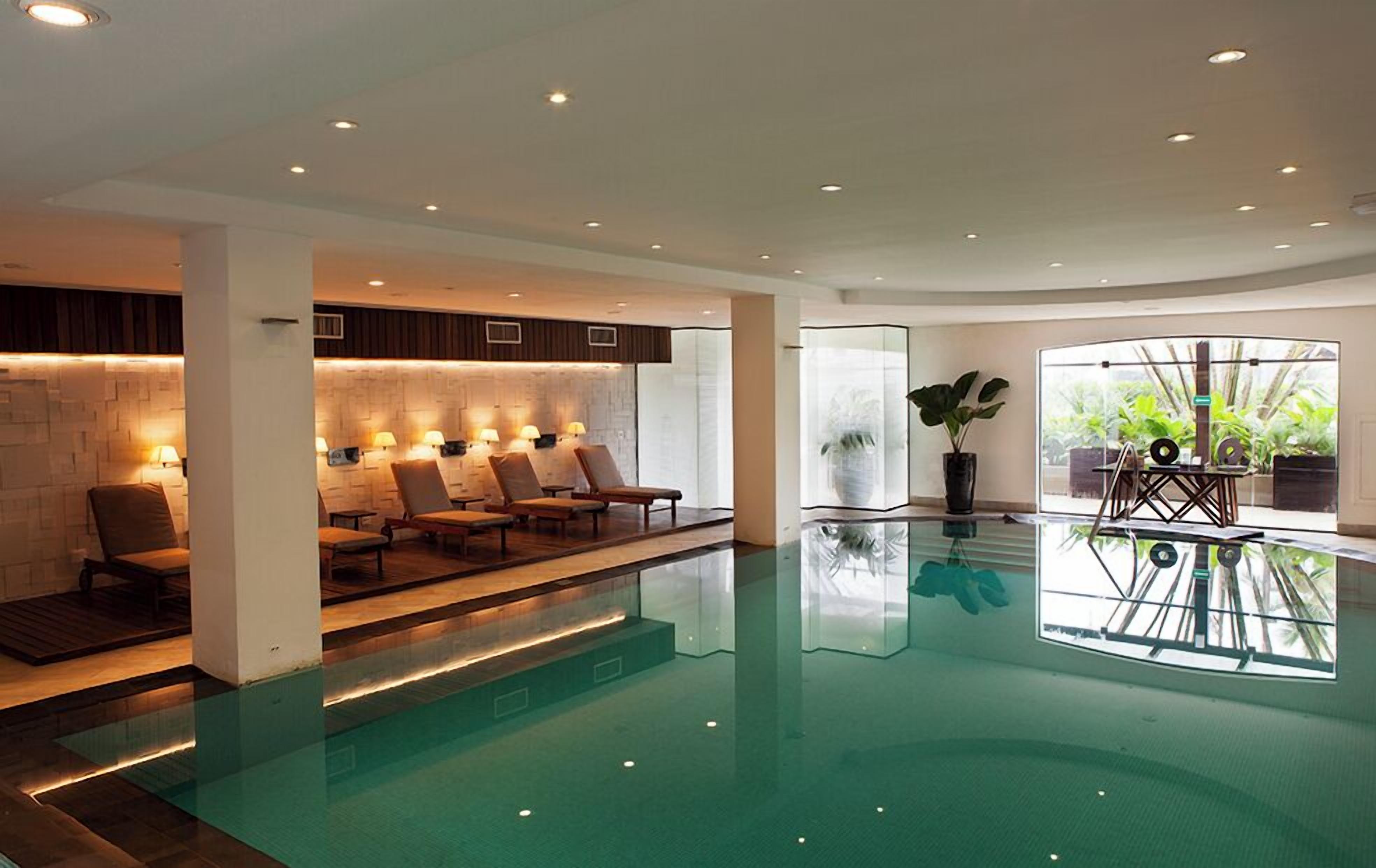 A modern indoor pool area with lounge chairs, a glass barrier, and a view of greenery outside.