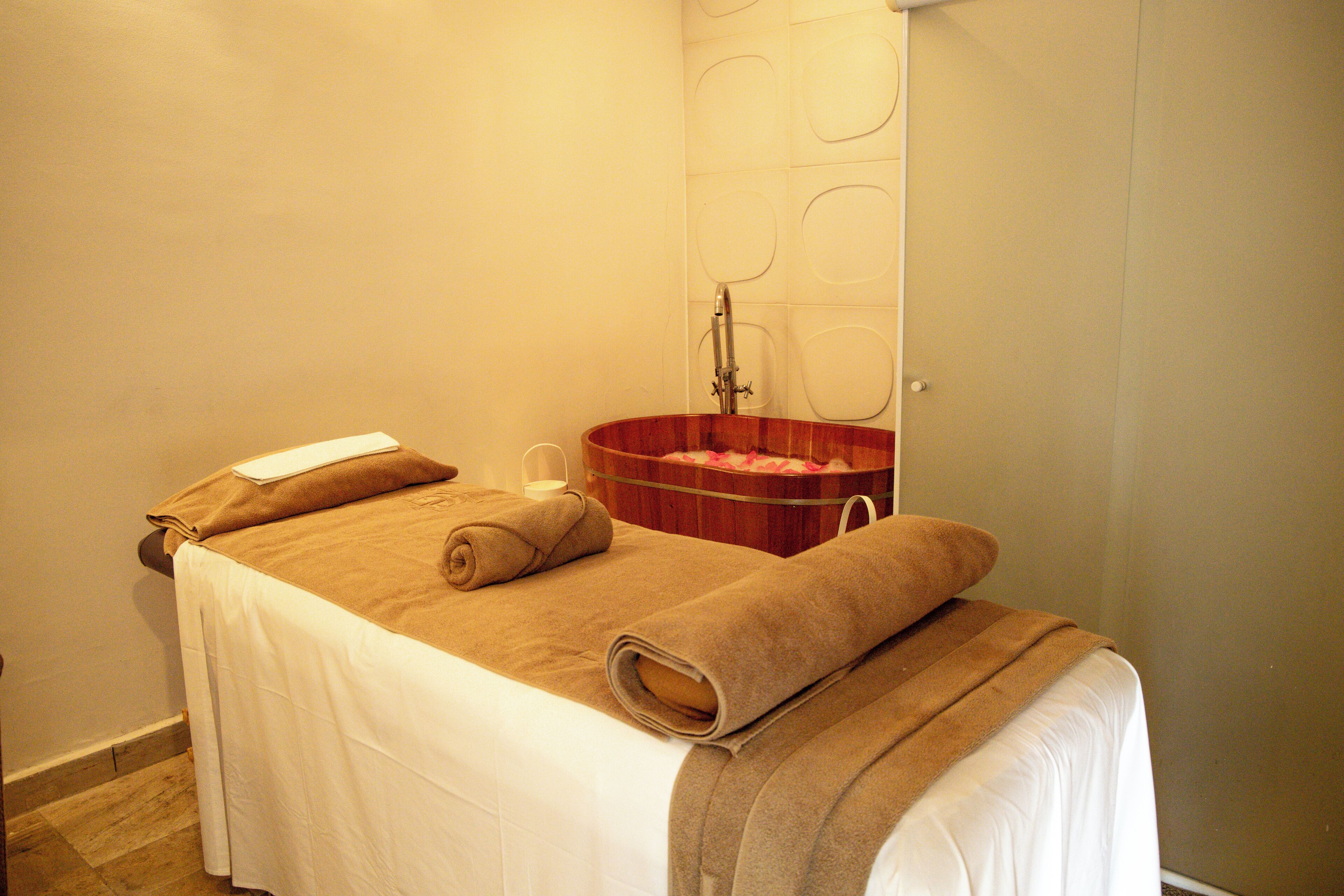 Ein Zimmer mit einem Bett, das mit einer weißen Bettdecke und braunen Handtüchern bezogen ist, einem Holzwaschbecken und einem Spiegel an der Wand.