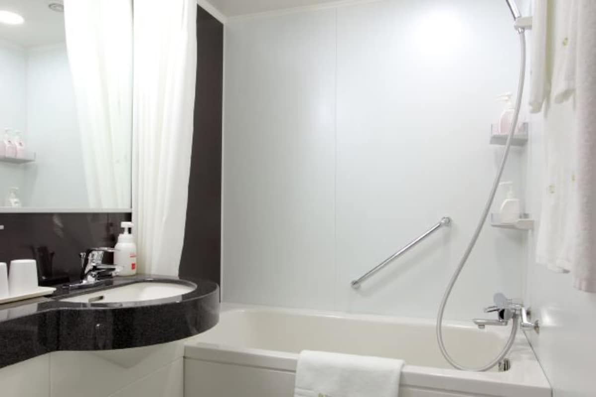 Une salle de bain moderne avec un lavabo sur un plan de toilette noir, une baignoire blanche et une douche équipée d’une barre d’appui.
