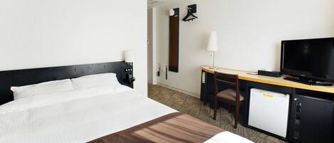 Quarto de hotel com cama, escrivaninha, computador, televisão e mini-frigorífico.