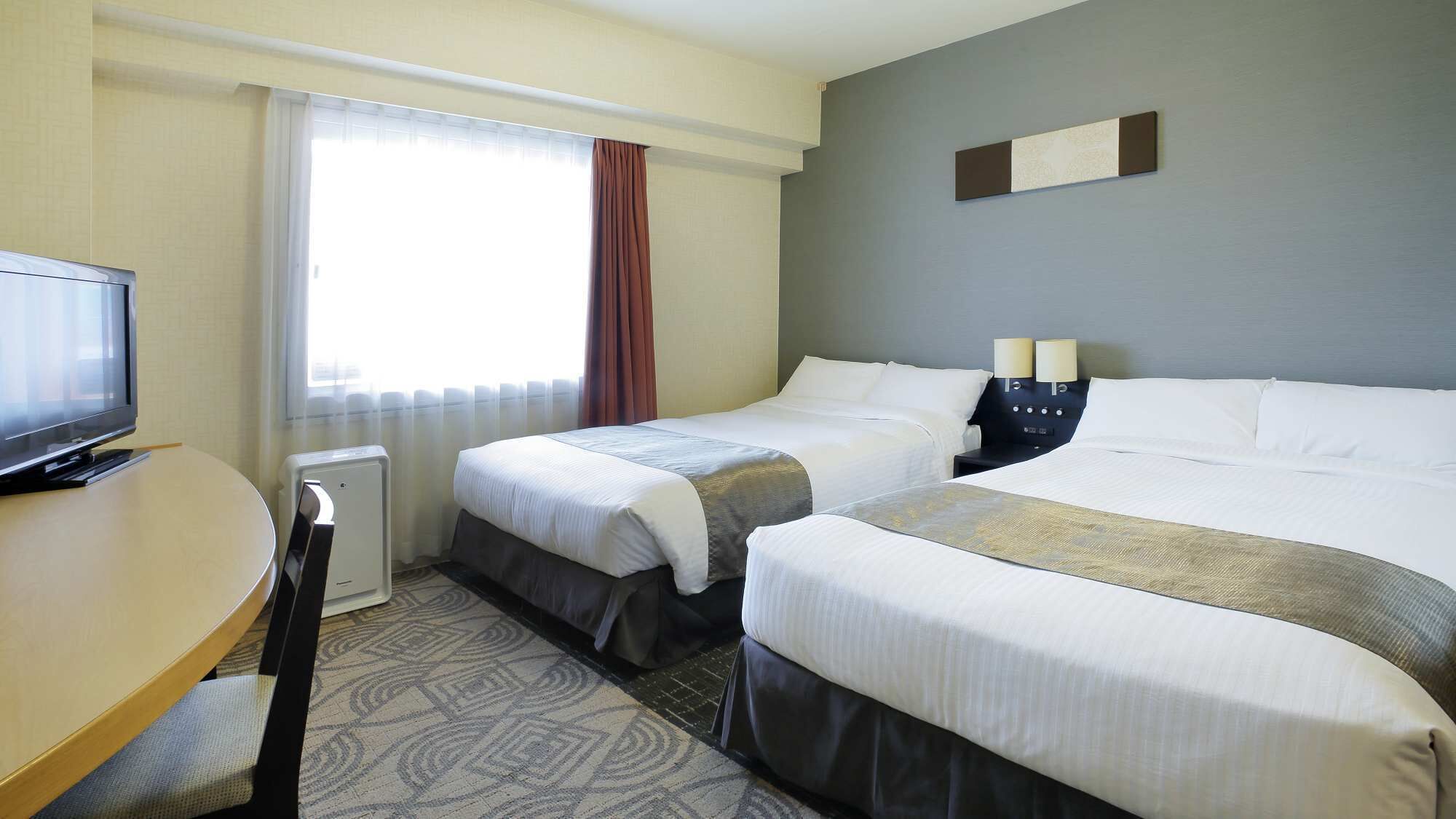 A hotel room with two beds, a desk, a television, and a window with curtains.