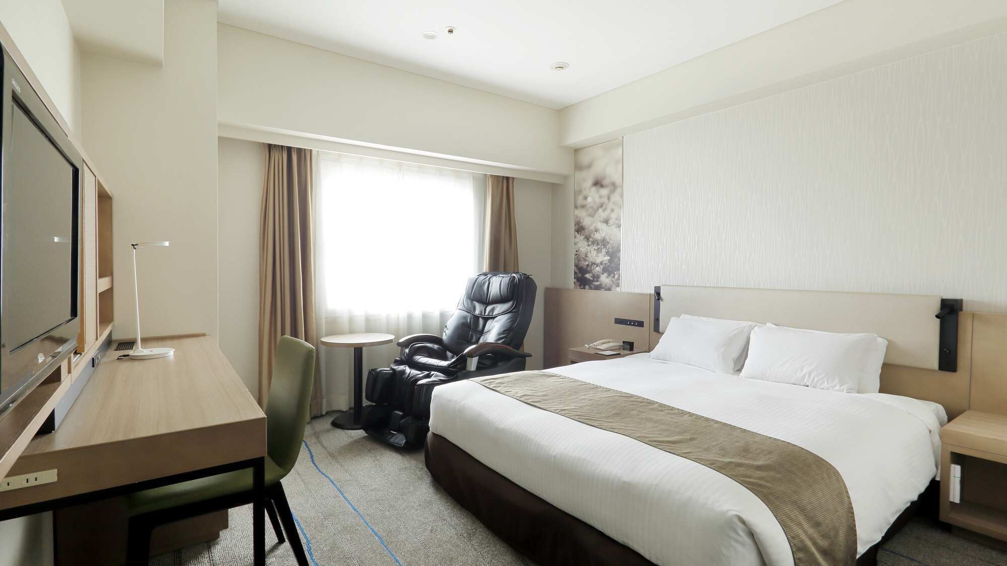 A hotel room with a bed, a desk, a chair, a massage chair, a TV, and a window with curtains.