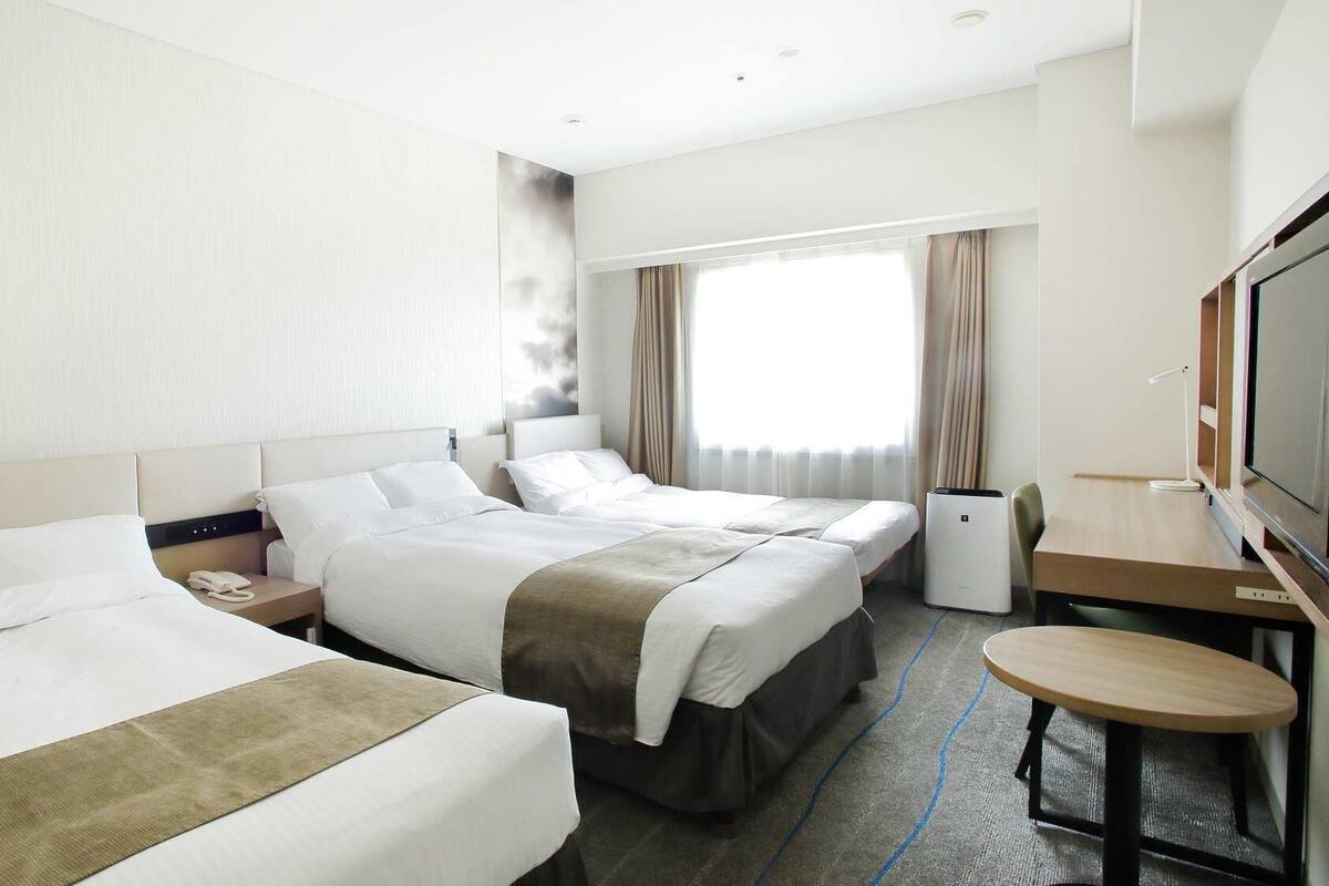 A hotel room with two beds, a desk, a TV, and a window with curtains.