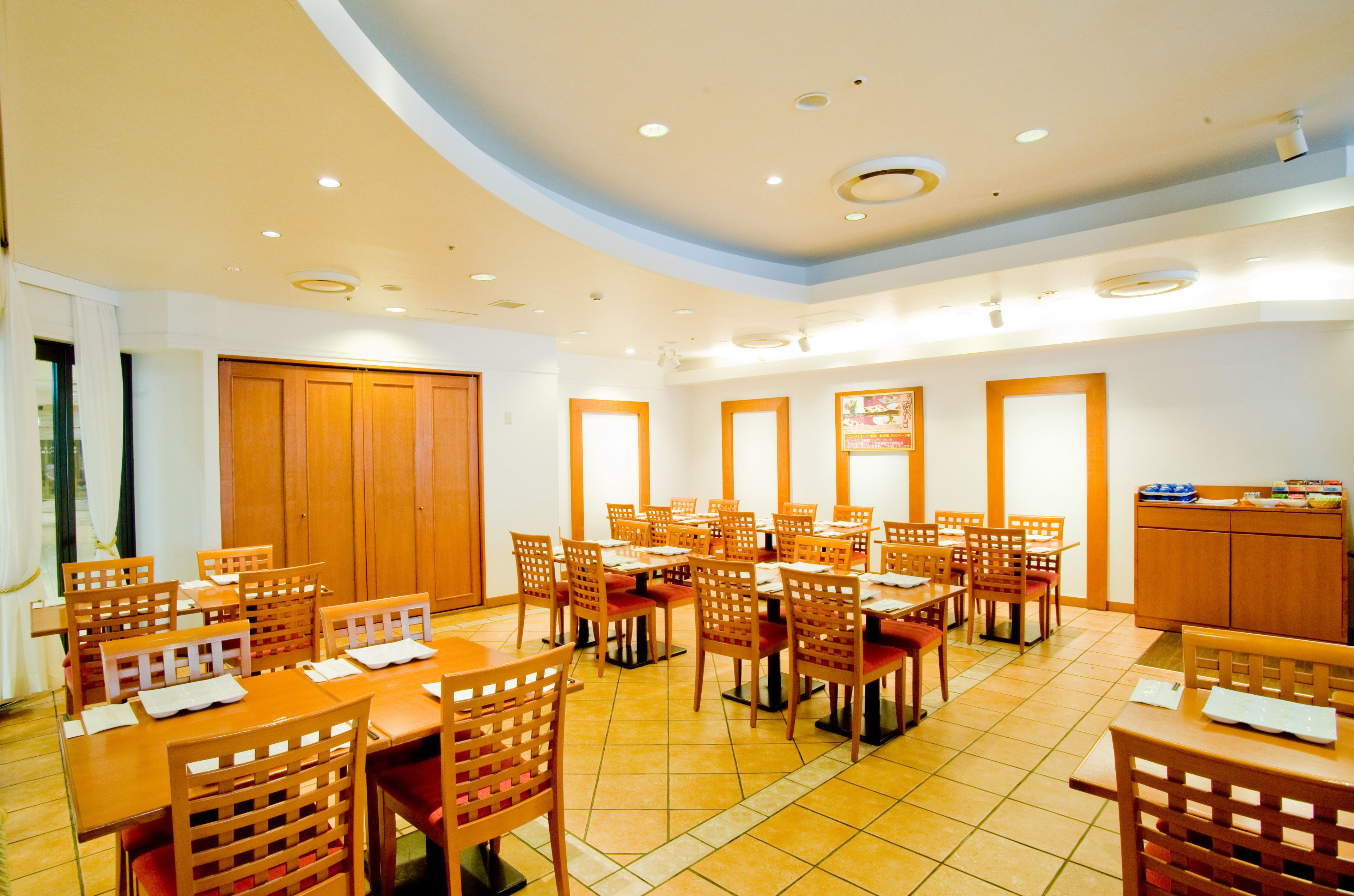 A dining area with multiple tables and chairs, wooden cabinets, and a tiled floor.