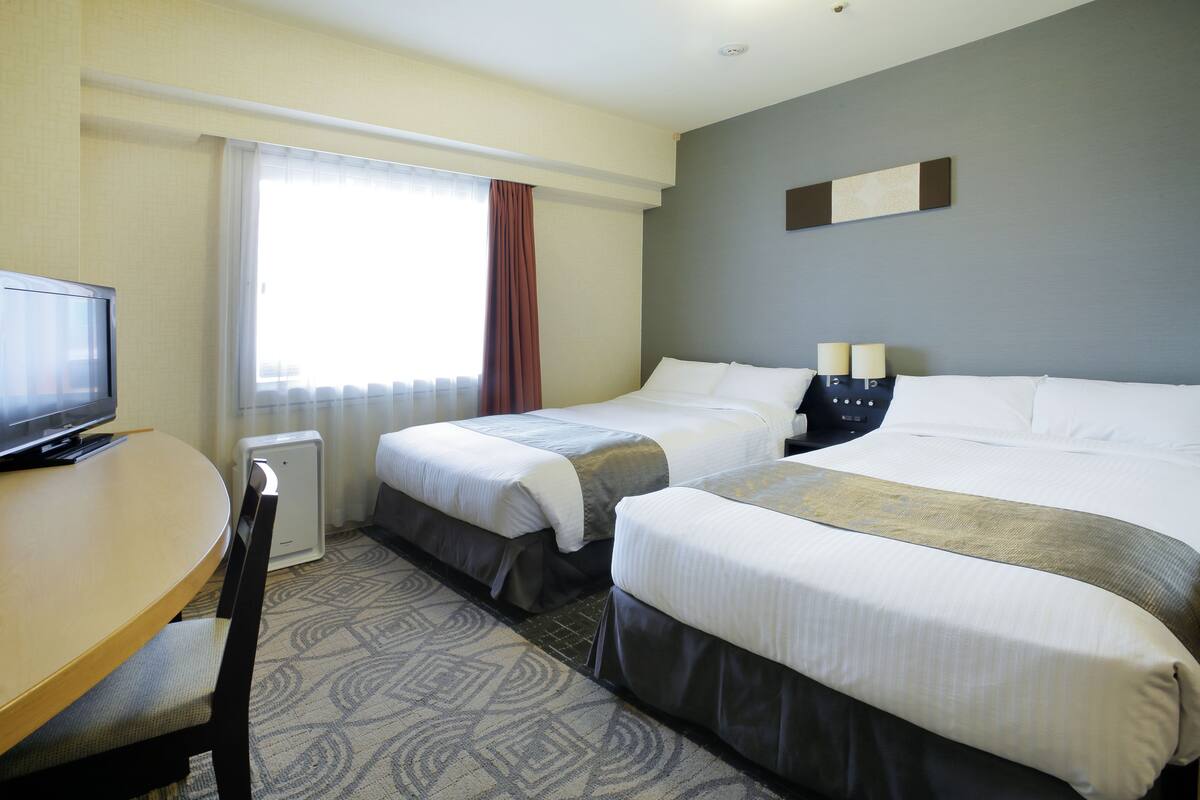 A hotel room with two beds, a desk with a television, and a window with curtains.
