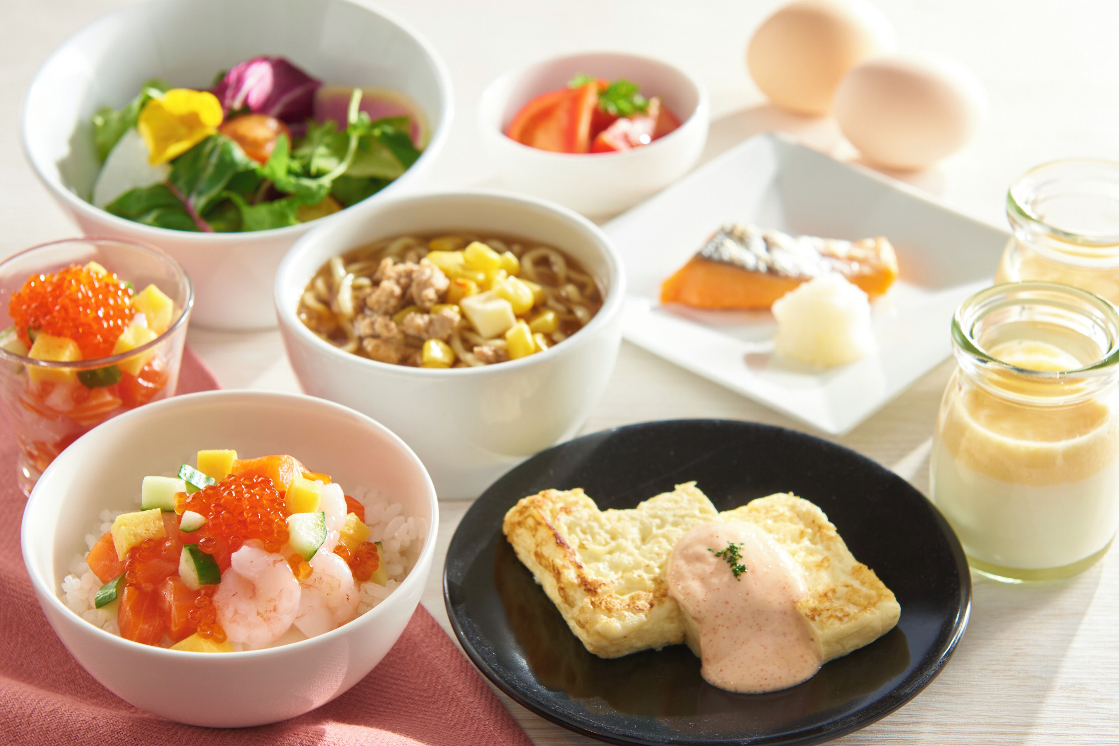 A table with various dishes including a bowl of rice with shrimp and vegetables, a bowl of soup, a plate with bread and butter, and a glass of milk.