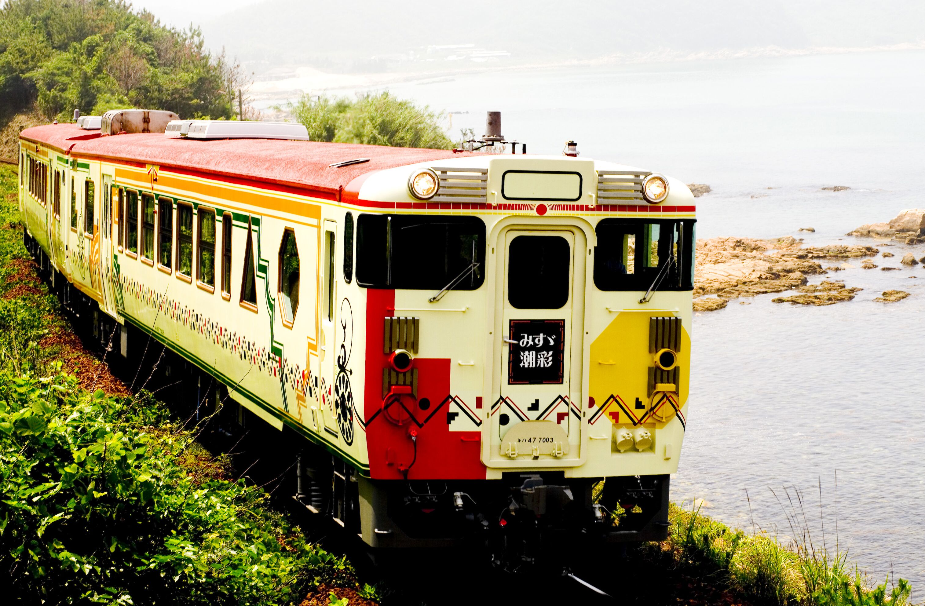 A vintage train with a red roof and green trim, parked by a body of water.