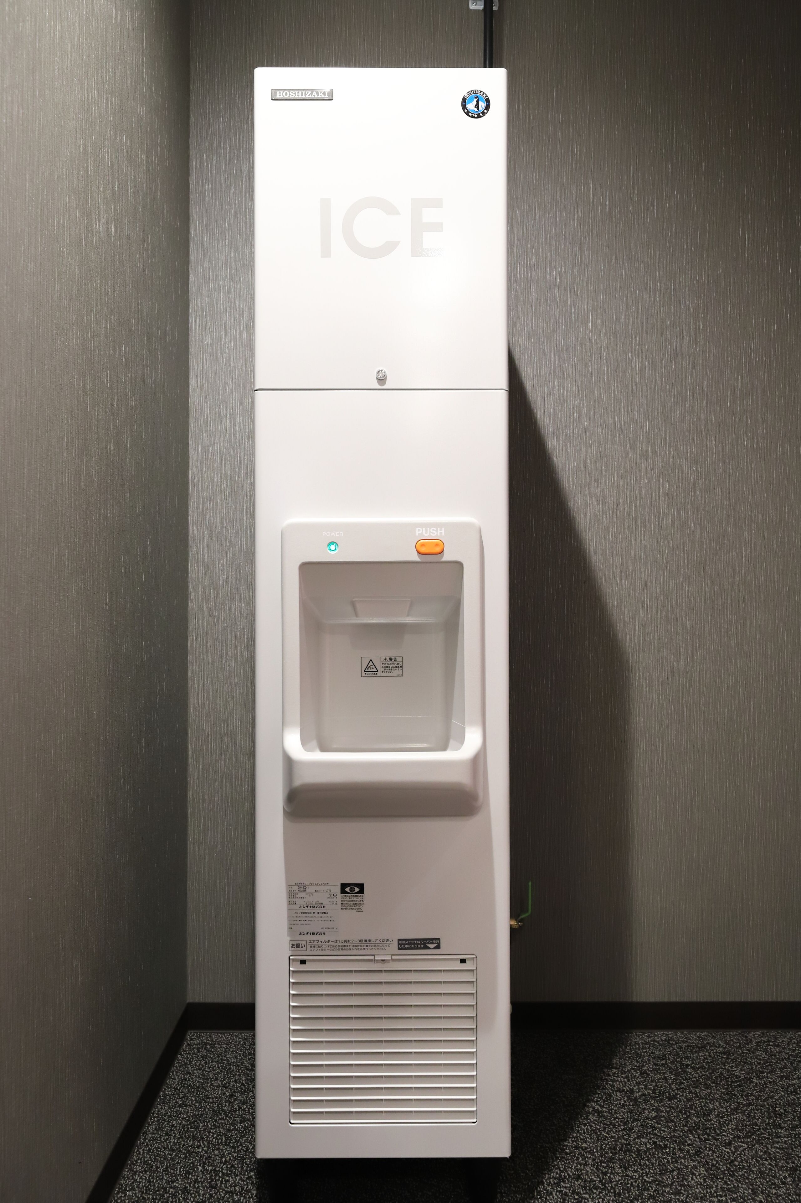 A hotel refrigerator with an ice dispenser, a push button, and a warning label.