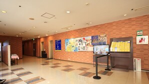 Un hall d’hôtel avec un sol carrelé, un comptoir d’accueil et des affiches d’information accrochées au mur.