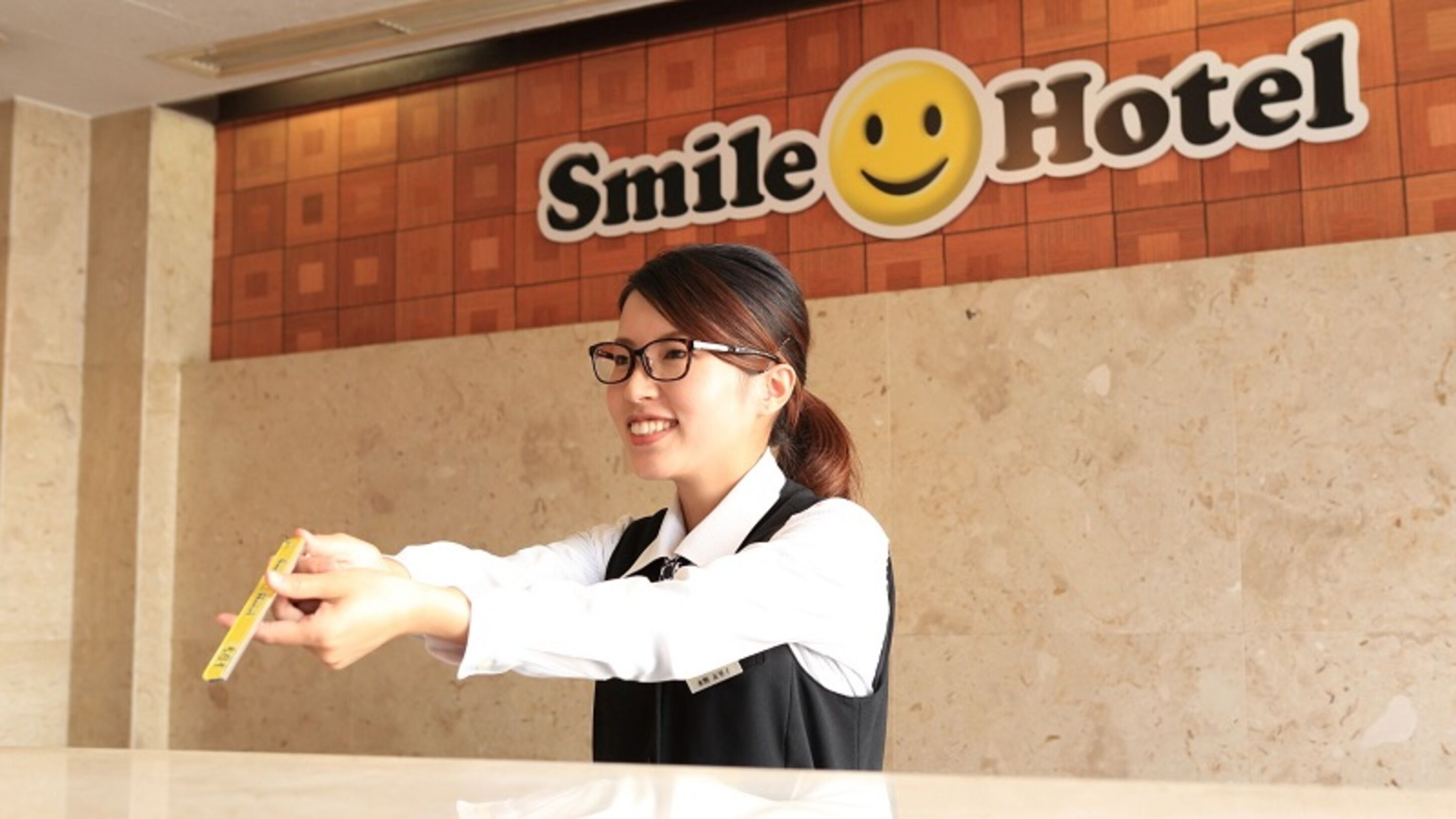 A person at a reception desk with a sign above reading "Smile Hotel".