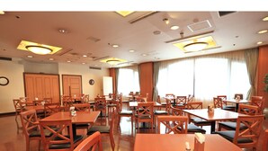 Un vaste espace dédié à la salle à manger, avec de nombreuses tables et chaises en bois, de grandes fenêtres dotées de rideaux et un plafond pourvu d’un éclairage encastré.