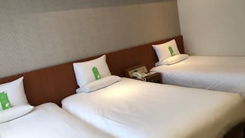 A hotel room with three single beds, each with white bedding and green pillows. There is a wooden headboard, a bedside table with a telephone, and a wall with a textured pattern.