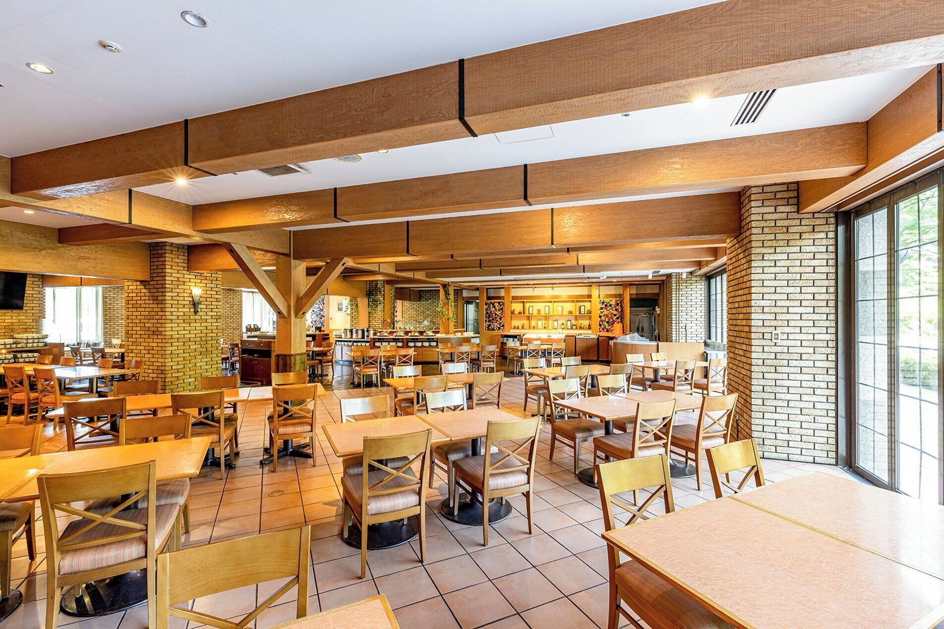 Un ristorante spazioso con numerosi tavoli e sedie, una parete in mattoni e un'ampia finestra che lascia entrare luce naturale.