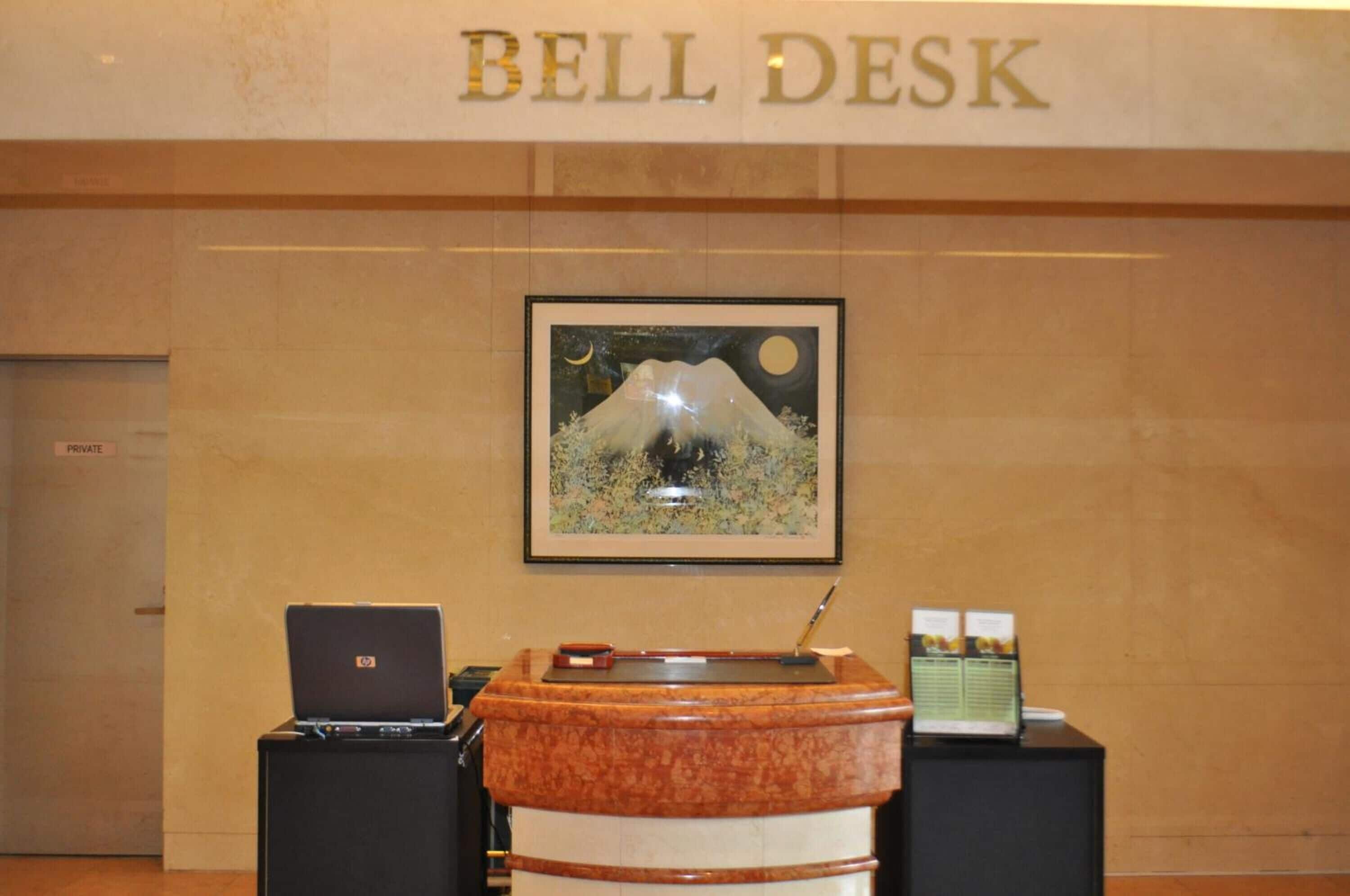 Een bell desk met een laptop, een ingelijst berglandschap en een prikbord.