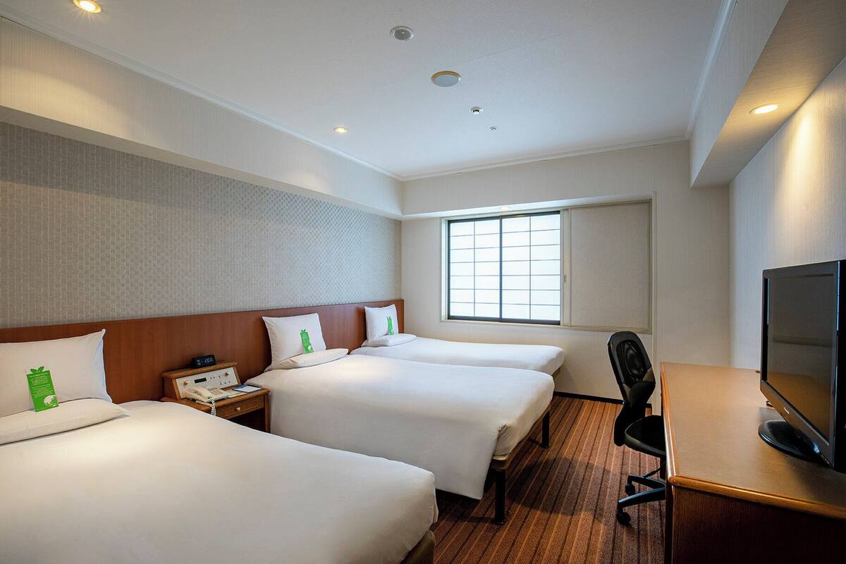 A hotel room with two beds, a desk, a television, and a window.