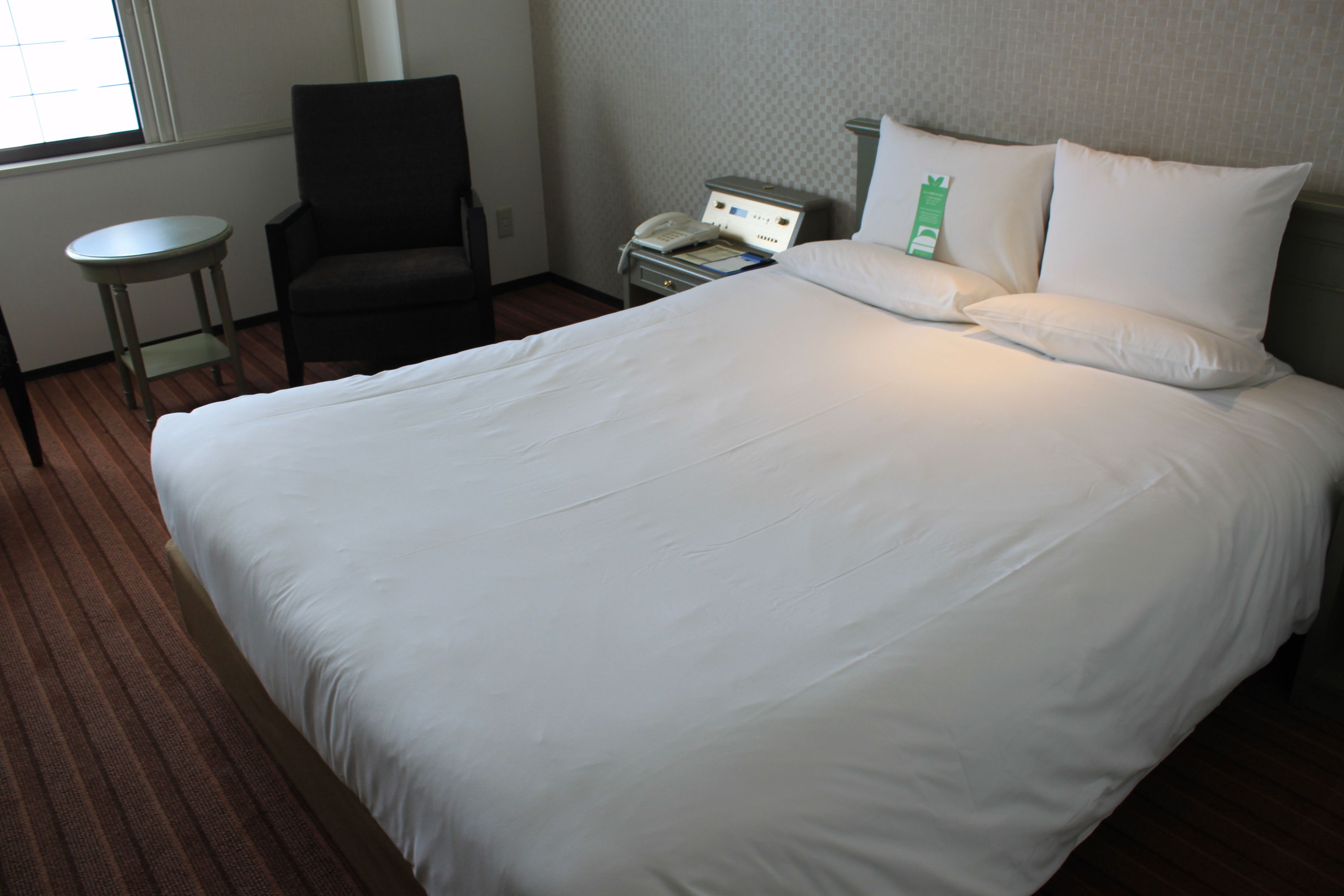 Una habitación de hotel con una cama grande, una silla, una mesita de noche y un teléfono.