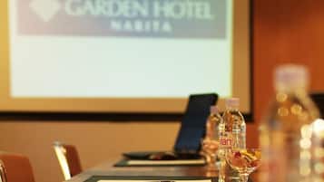 Sala de conferência com uma mesa comprida, garrafas de água e uma tela de projeção exibindo o logotipo do Garden Hotel.