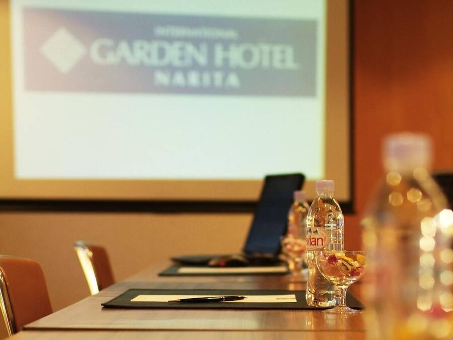 Sala de conferência com uma mesa comprida, garrafas de água e uma tela de projeção exibindo o logotipo do Garden Hotel.