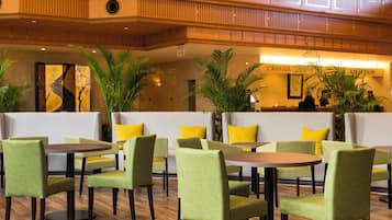 Eine Hotelhalle mit grünen Polstersesseln, Holztischen und Blumentöpfen.