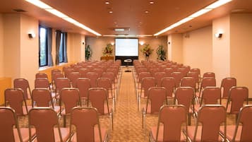 A conference room with rows of chairs, a projector screen, and a carpeted floor.