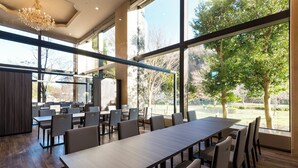 A conference room with a long table and multiple chairs, large windows with a view of trees and a fence, and a chandelier. - International Garden Hotel Narita (Narita)