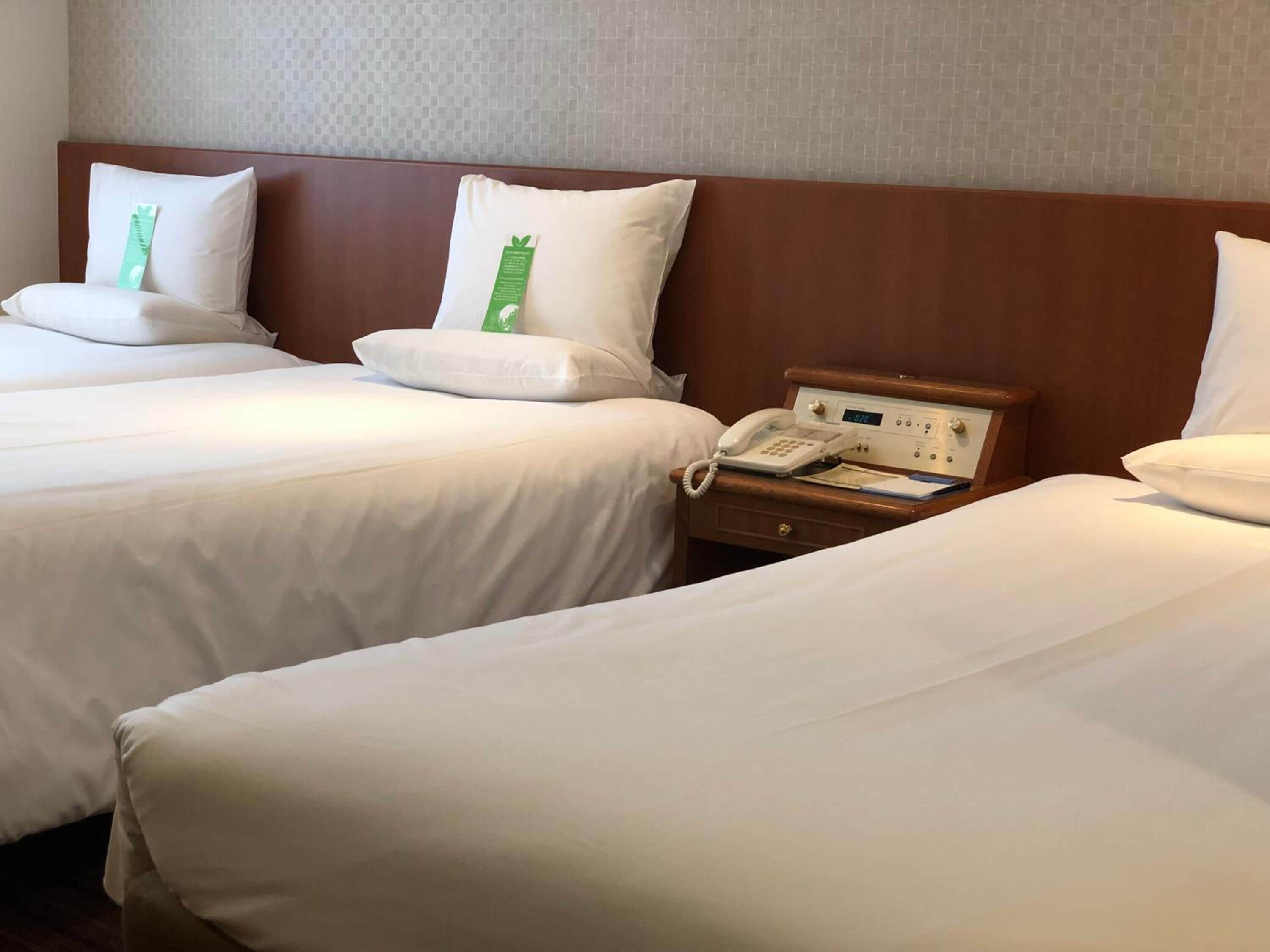 A hotel room with two beds, each with white linens and pillows, a wooden headboard, and a bedside table with a telephone and a notepad.
