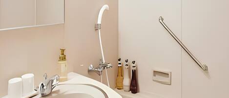 Un baño con lavamanos blanco, espejo, ducha y barandilla.