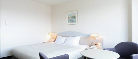 A hotel room with a bed, two bedside tables with lamps, a small round table, and two chairs.