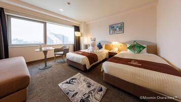 A hotel room with two beds, a desk, a chair, a window with a city view, and a small table with a lamp.