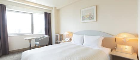 Habitación de hotel con una cama grande, un escritorio, una silla, una mesita de noche y una lámpara de pared.