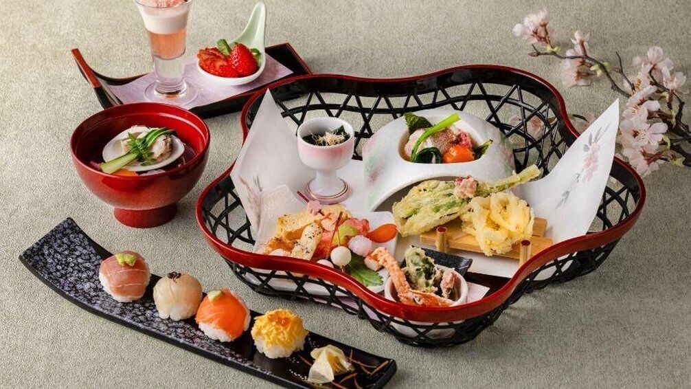 A variety of Japanese dishes including sushi, sashimi, and tempura, served on a tray with a decorative basket.