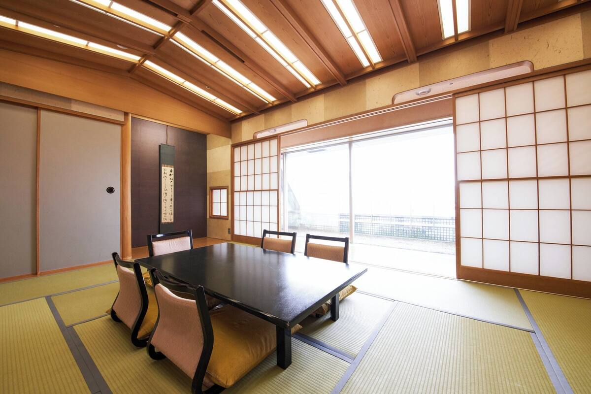 A traditional Japanese room with tatami flooring, a low table with cushions, sliding doors, and a view through a shoji screen.