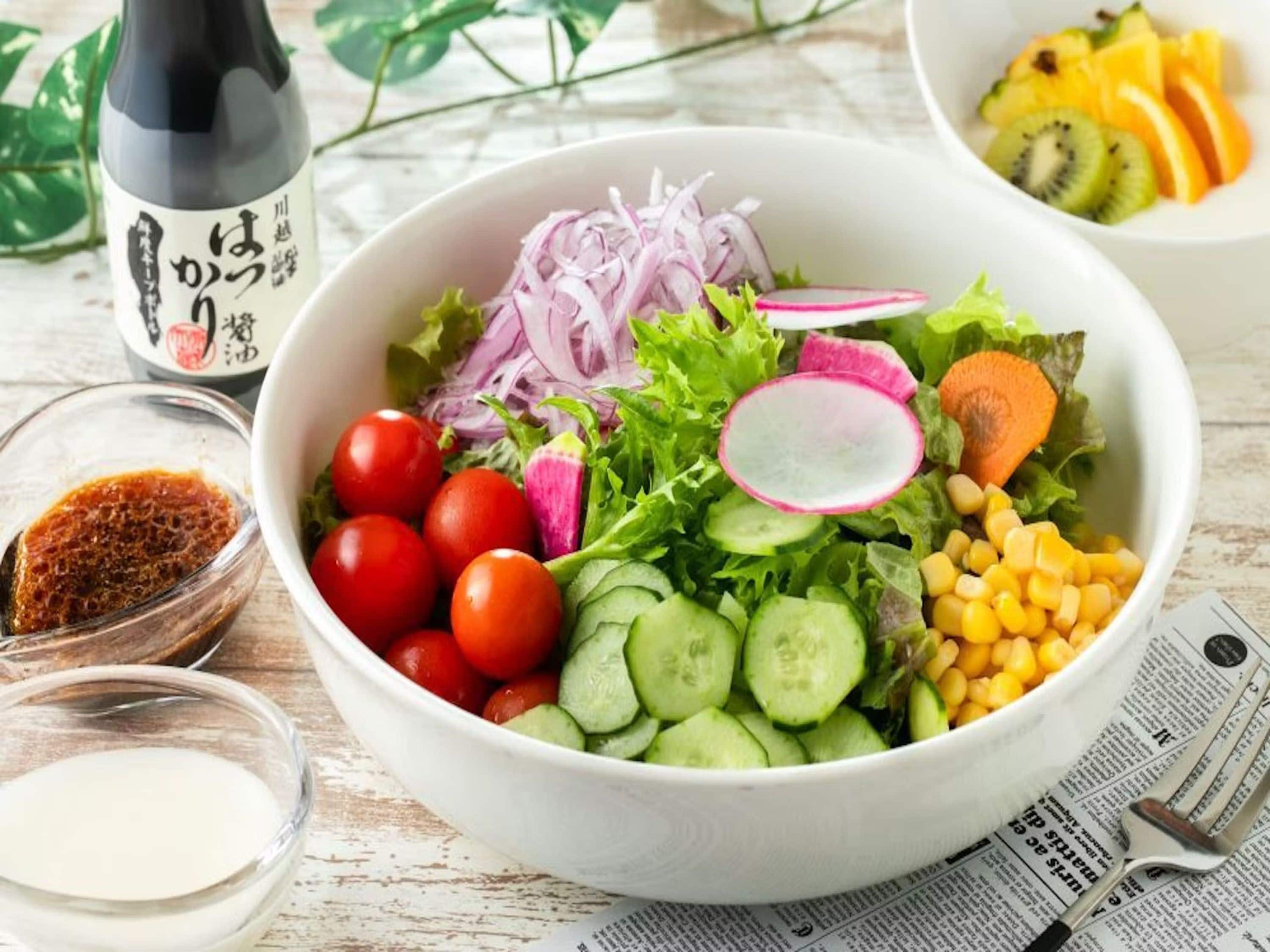 A bowl of salad with various vegetables and a bottle of sauce.