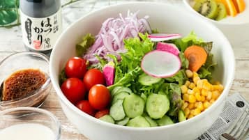 A bowl of salad with various vegetables and a bottle of sauce.