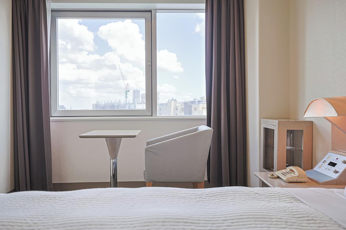 Ein Hotelzimmer mit Bett, Schreibtisch, Stuhl, Fenster mit Stadtblick und Telefon auf dem Schreibtisch.