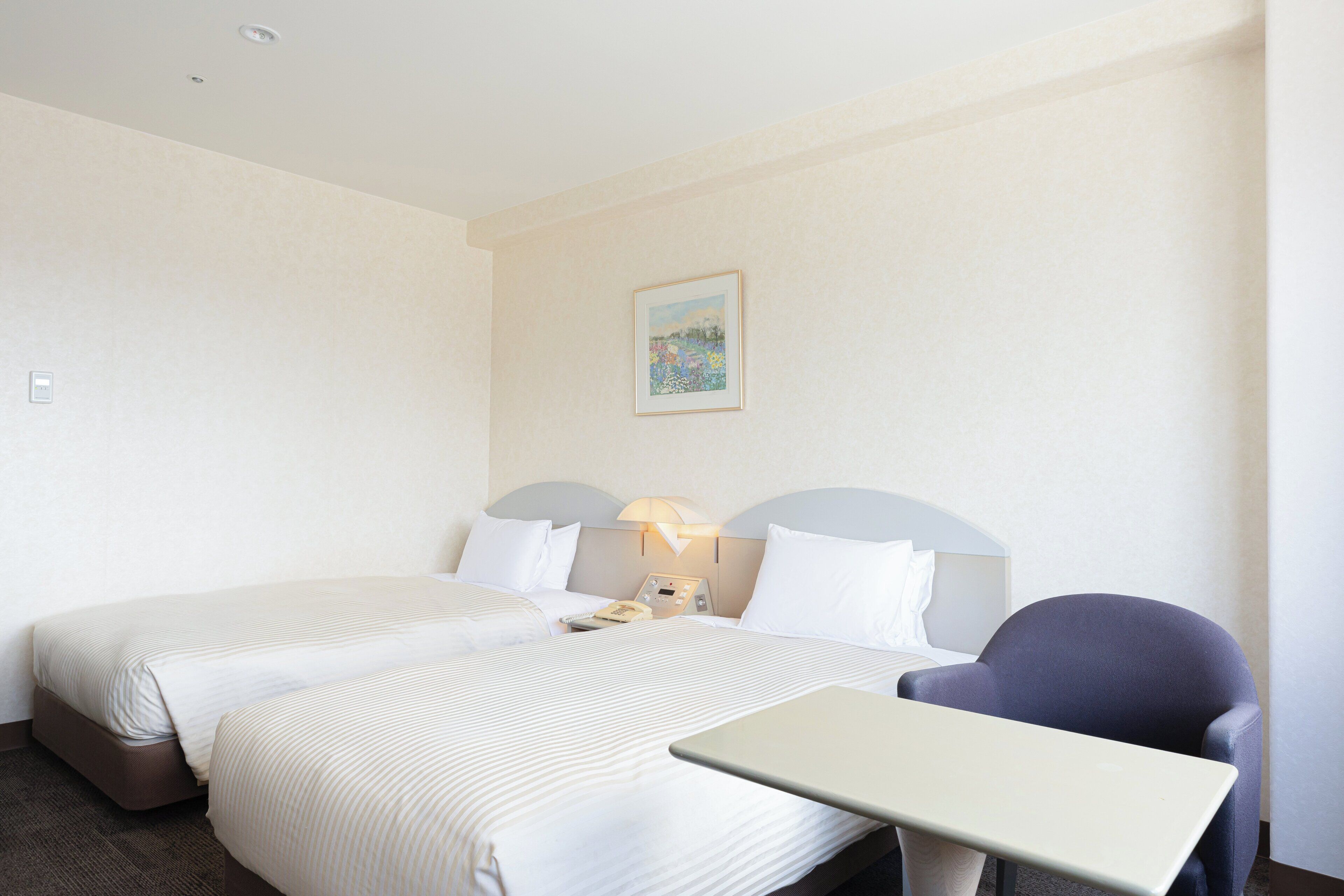 Ein Hotelzimmer mit zwei Betten, einem Schreibtisch, einem Stuhl, einer Lampe und einem Bild an der Wand.