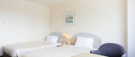 Ein Hotelzimmer mit zwei Betten, einem Schreibtisch, einem Stuhl, einer Lampe und einem Bild an der Wand.