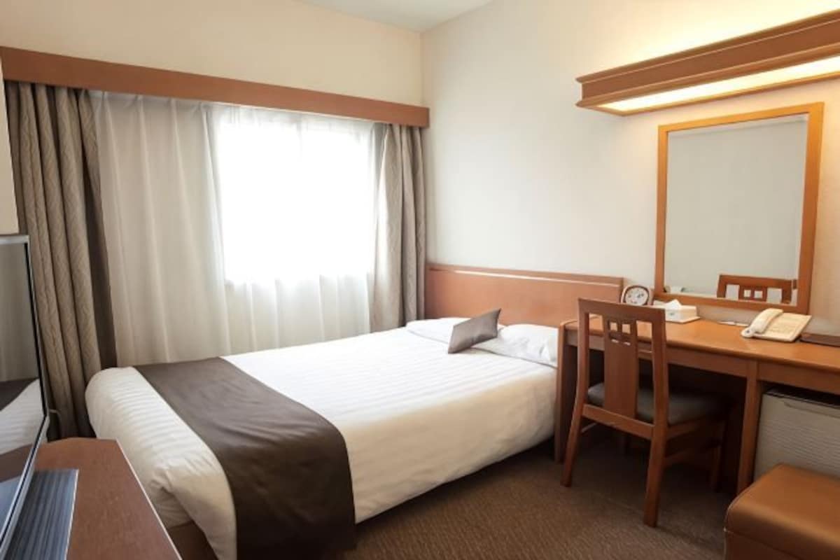 Quarto de hotel com cama, escrivaninha, cadeira e um espelho grande.