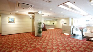 Un vestíbulo de hotel con alfombra roja, mostrador de recepción y una planta en maceta.