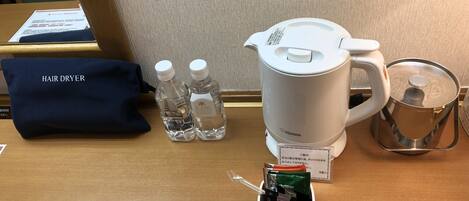 Una habitación de hotel con secador de pelo, dos botellas de agua, cafetera y tetera sobre la mesa.