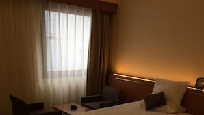 Una habitación de hotel con dos camas, un escritorio, una silla y un ventanal con cortinas.