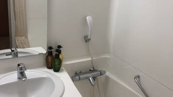 A bathroom with a white sink, a mirror, a shower with a handheld showerhead, and a grab bar.