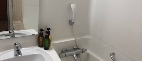 Un baño con lavamanos blanco, un espejo, ducha con cabezal de ducha de mano y barra de apoyo.