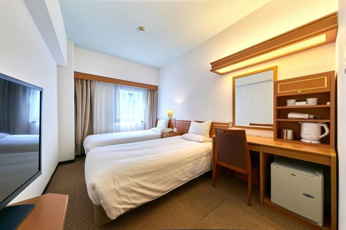 A hotel room with two beds, a desk, a chair, a television, a mini-fridge, and a mirror.