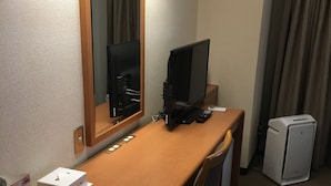Habitación de hotel con un escritorio de madera, un televisor de pantalla plana, una cafetera, un refrigerador pequeño y un espejo.