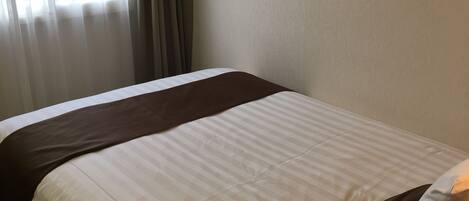 A hotel room with a bed, a wooden nightstand, and a window with curtains.