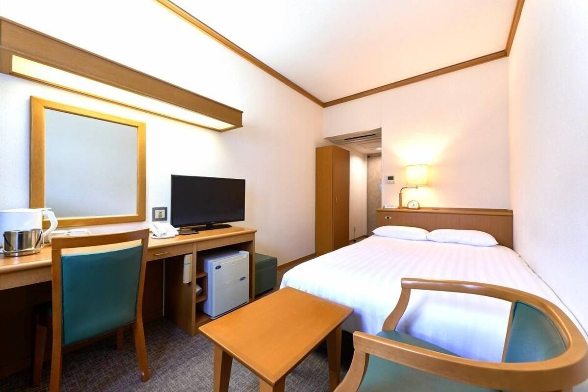 A hotel room with a bed, desk, chair, television, and a small refrigerator.
